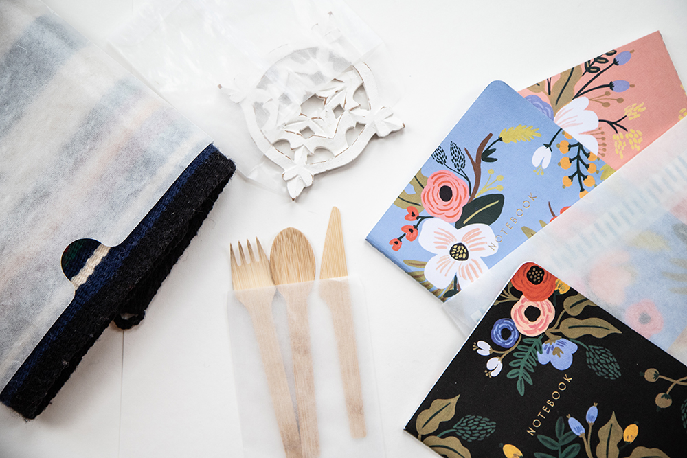 A display of packaging for online stores shows glassine bags containing a variety of products like floral notebooks, wooden utensils, and a decorative wooden snowflake.