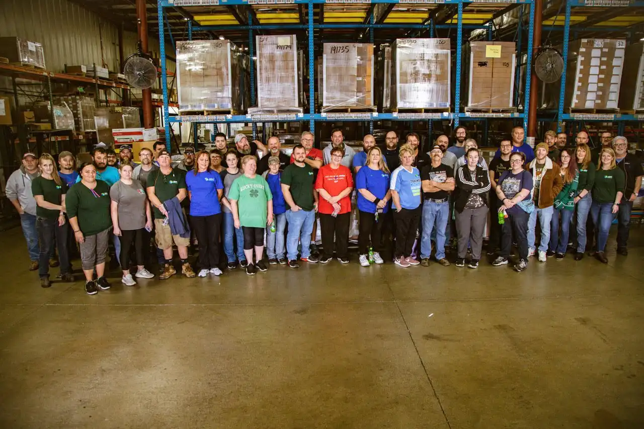 Big group of JBM team members standing together in packaging facility.