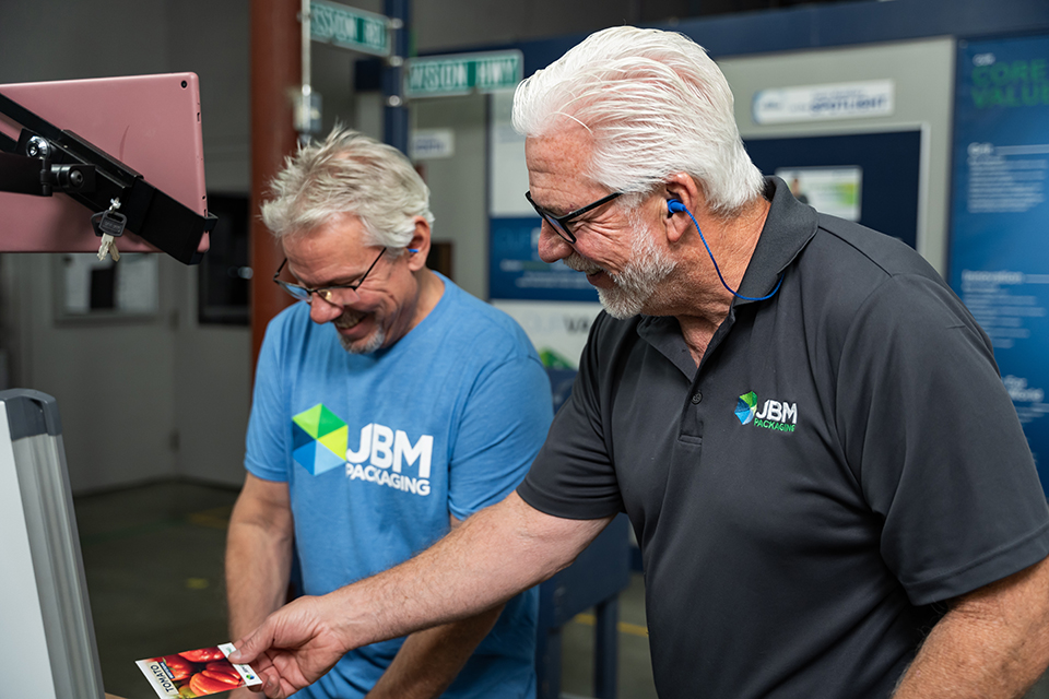 Two JBM team members smiling and looking at the quality of a seed packet.