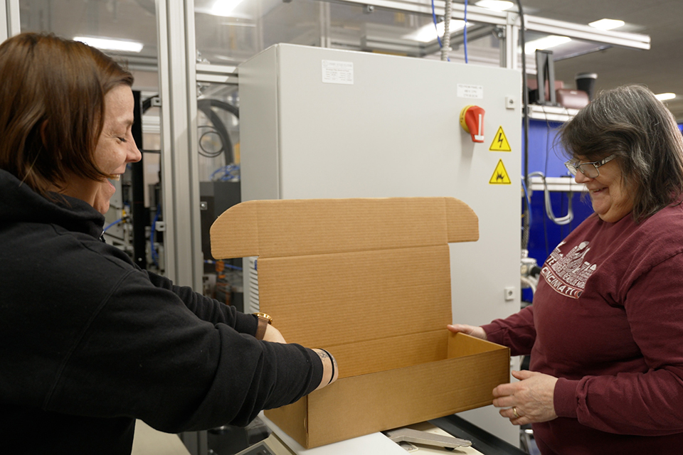Two team members, part of the second chance program at JBM Packaging, laugh and smile as they work on packaging.