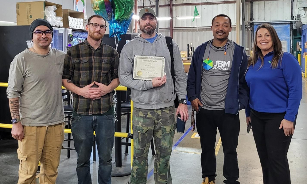 Group of operations team members standing togther smiling and celebrating the Fair Chance program at JBM Packaging.