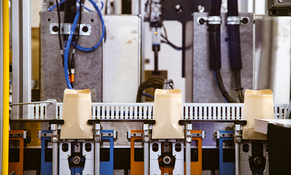 An automated filling machine shows kraft paper coin envelopes ready to be filled as part of the wholesale packaging fulfillment services available from JBM Packaging.