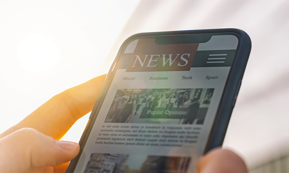 A person's hand holding a phone with a website that says "NEWS" on the screen