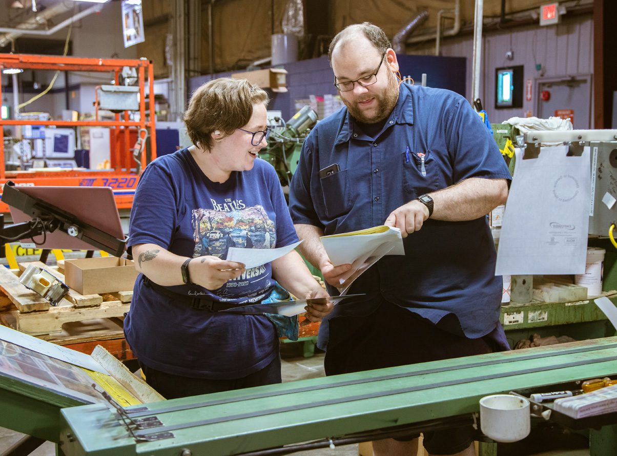 Two JBM team members smiling and looking at a piece of paper together in the packaging facility.