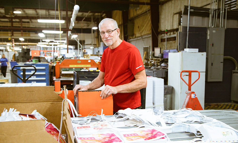 JBM employee smiling and working on custom paper packaging for a customer.